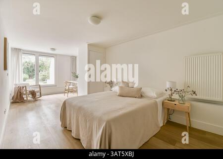 Ein helles, luftiges Schlafzimmer mit einem einfachen Bett, minimalistischer Einrichtung und großen Fenstern, die natürliches Licht ermöglichen. Die neutralen Töne schaffen eine friedliche Atmosphäre. Stockfoto