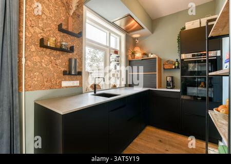 Eine stilvolle Küche mit eleganten schwarzen Schränken, einer metallischen Arbeitsplatte und natürlichem Licht unterstreicht die moderne Ästhetik. Stockfoto