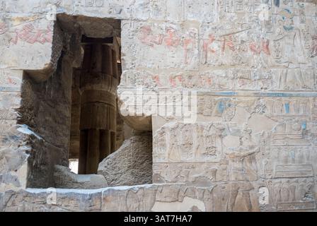 Antike ägyptische Tempelwand mit Hieroglyphen und Schnitzereien, die komplexe Designs und eine große Öffnung zeigen, die ein säulenförmiges Inneres freigibt. Stockfoto
