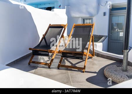 Zwei schwarze Liegestühle auf einer sonnigen Terrasse in Imerovigli Santorini mit weißer Kykladen-Architektur und einem kleinen Tauchbecken in der Ecke in der Nähe eines grauen Do Stockfoto