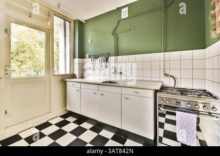 Eine elegante Küche mit grüner Wand, kariertem Boden und modernen Geräten. Das geräumige Layout verbessert Funktionalität und Stil. Stockfoto