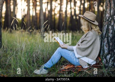 Frau, die im Wald Buch liest. Entspannung in der Natur zur Verbesserung der psychischen Gesundheit. Waldtherapie Stockfoto