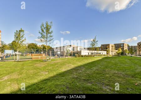 Ein lebhafter Stadtpark mit üppigem Gras, gepflegten Bäumen und einem Spielplatz bietet eine ruhige Umgebung inmitten moderner Architektur. Stockfoto