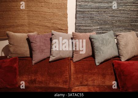 Eine in warmen Farben gehaltene Sitzanordnung mit einem rostfarbenen Cordsofa, das mit verschiedenen strukturierten Kissen in gedämpften Tönen wie Beige und Malve verziert ist Stockfoto