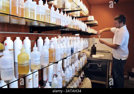 24. Juli 2013 – Charlotte, NC, USA – nachdem Nikotin aus dem Nikotinspender (brauner Behälter auf dem Tisch) in eine Flasche gegeben wurde, fügt MadVapes Store Manager Robert Everhart aromatisiertes E-Liquid hinzu (verschiedene Geschmacksrichtungen sind in den Flaschen mit e-Liquid im Vordergrund zu sehen) und druckt ein Etikett ab, das auf die Flasche aufgeklebt wird. Das Gemisch wird dann in den unteren gewickelten Tank der elektronischen Zigarette gegeben. Elektronische Zigaretten werden immer beliebter, aber landesweit gibt es noch immer Bedenken hinsichtlich ihrer Sicherheit. E-CIG-Kultur umfasst „Vaping“-Treffen und eine Reihe von Produkten, die sich selbst zusammenstellen. (Cr Stockfoto