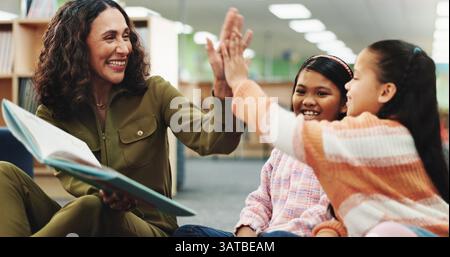 Schulkinder, Lehrer und High Five mit Buch in der Bibliothek für Leistung, Lernen und Feiern für Fortschritt. Kinder, Lesen und Geschichte mit der Frau Stockfoto