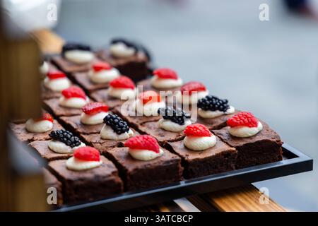 Köstliche Schokoladen-Brownie-Quadrate, garniert mit Schlagsahne und frischen Beeren, bereit für eine Veranstaltung mit Catering Stockfoto