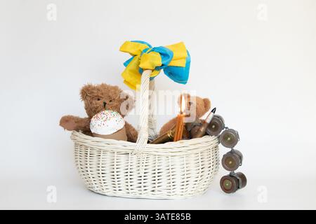 Die Flagge der Ukraine wickelt sich um den Griff eines Korbs, der einen Osterkuchen und Kinderspielzeug, Kartuschen und Kerzen auf einem weißen Korb enthält Stockfoto