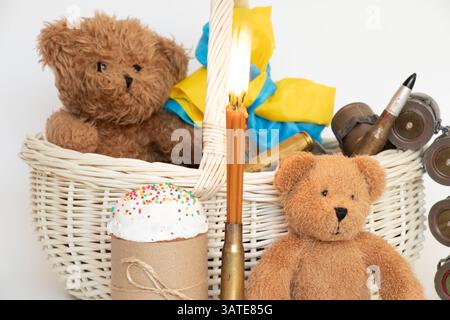 Die Flagge der Ukraine wickelt sich um den Griff eines Korbs, der einen Osterkuchen und Kinderspielzeug, Kartuschen und Kerzen auf einem weißen Korb enthält Stockfoto