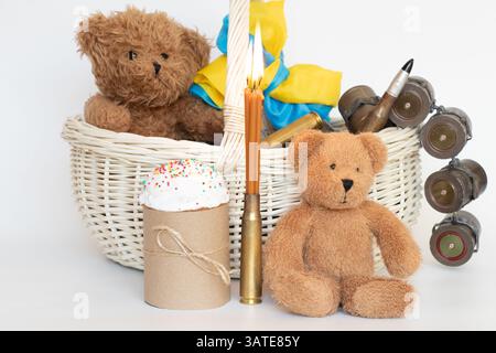 Die Flagge der Ukraine wickelt sich um den Griff eines Korbs, der einen Osterkuchen und Kinderspielzeug, Kartuschen und Kerzen auf einem weißen Korb enthält Stockfoto