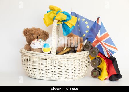 Osterkorb mit Bären und Fahnen Deutschlands und der Ukraine, der Europäischen Union, Großbritanniens und Kugeln und Granatwerfer auf weißem Hintergrund, Stockfoto