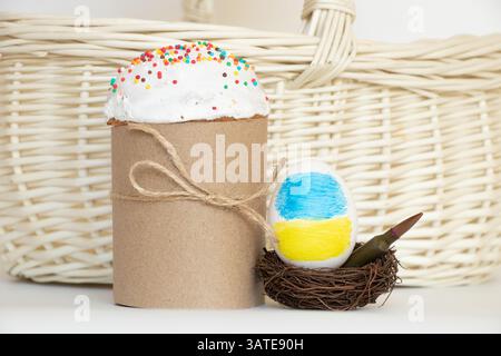 Die Flagge der Ukraine wird auf ein Ei gezeichnet, das in einem Nest mit einer Kugel liegt und daneben befindet sich ein Osterkuchen in der Nähe eines Korbkorbs, Ostern in der Ukraine Stockfoto