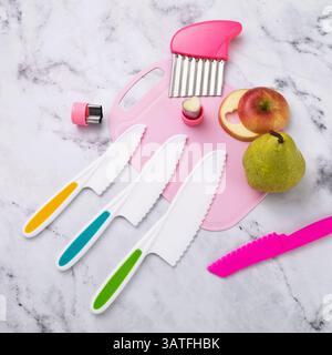 Satz verschiedener Messer, Kunststoff und Edelstahl, rosafarbenes Schneidebrett und geschnittene ​​fruits auf dem Tisch, Draufsicht Stockfoto
