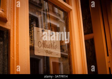 Madrid, Spanien 1. Mai 2024 Ein hölzernes Schild im Fenster mit der Aufschrift „Aberto“ (auf Portugiesisch, Spanisch geöffnet), das von einem orangen Gebäude umgeben ist, das bereit ist für den Geschäftsbetrieb Stockfoto