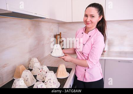 Moskau, Russland, 18.04.25. Eine Frau in einem rosafarbenen Mantel hält ein Tablett mit Gebäck. Sie lächelt und ist stolz auf ihre Arbeit Stockfoto