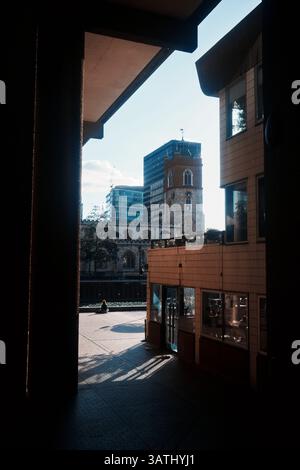 London, Großbritannien - 28. September 2024: Eine Frau geht durch einen schattigen Durchgang im Barbican Estate, mit der St Giles Cripplegate Church darüber hinaus Stockfoto