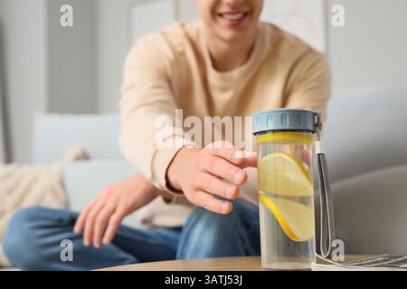 Hübscher junger Mann, der zu Hause nach einer Flasche Zitronenwasser greift Stockfoto