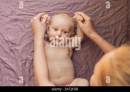 Das Neugeborene liegt auf einer weichen Decke, während die Mutter die kleinen Gliedmaßen des Babys sanft anübt. Frühentwicklung, Bindung und Babypflegekonzept Stockfoto