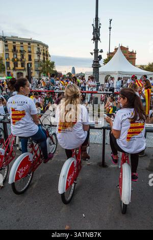 Sep 11, 2015 - Barcelona, Spanien - 3 Frauen draufsetzen Leihfahrräder vorgeschlagenen Catalonia Karte auf Shirts zu tragen. Menschen März tragen die katalanische Flagge, um den Arc de Triomf in Barcelona. Barcelona war ein Meer von rot und gelb wie Massen mit separatistischen Fahnen marschierten in der Stadt, katalanischen Nationalfeiertag zu feiern. Organisatoren hoffen, mindestens 500.000 Menschen für eine pro-Unabhängigkeit-Rallye unter dem Motto "Fangen wir bauen ein neues Land". Die Estelada oder "lone star Flag" ist eine inoffizielle Flagge typisch katalanischen Separatisten ihre Unterstützung für ein unabhängiges Katalonien zum Ausdruck bringen. (Credi Stockfoto