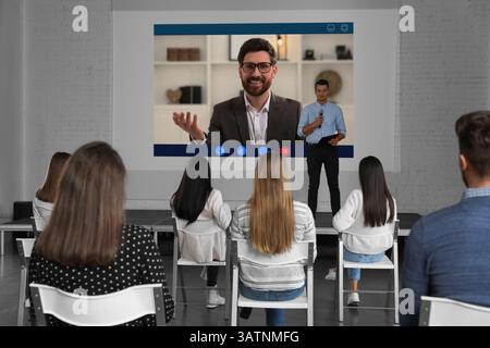 Redner, der über Online-Videochat an der Vorlesung teilnimmt. Publikum und Trainer im Konferenzraum mit Projektionsleinwand Stockfoto