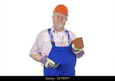 Maurer in blauer Latzhose und Helm hält Kelle und Ziegel in der Hand Stockfoto