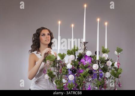 Junge, schöne Frau, die neben dem großen geschmückten Leuchter steht Stockfoto