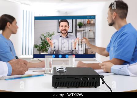 Redner, der über Online-Videochat an der Vorlesung teilnimmt. Medizinisches Personal im Konferenzraum mit Projektionsleinwand Stockfoto