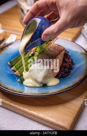 Koch gießt Sauce auf Lachssteak mit Gemüse und schwarzem Reis Stockfoto