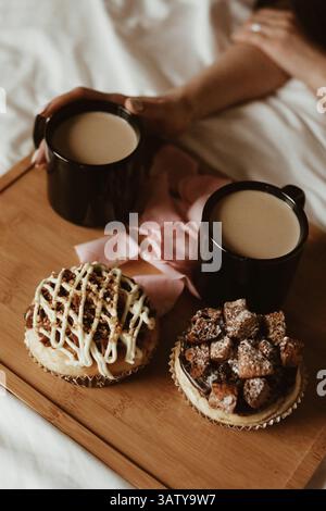 Frauenhände, zwei schwarze Tassen Kaffee mit Milch und köstliche süße Cupcakes mit Buttercreme und Keksen auf einem Holztisch Stockfoto