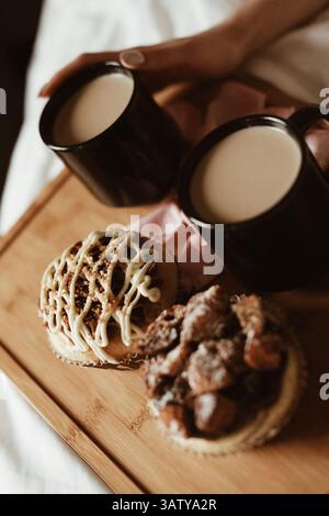 Frauenhände, zwei schwarze Tassen Kaffee mit Milch und köstliche süße Cupcakes mit Buttercreme und Keksen auf einem Holztisch Stockfoto