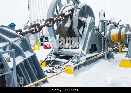 Das Anlegedeck eines Frachtschiffes mit Ankerwinden, einer Ankerkette an Winden, Pollern und Haws mit Anlegeseilen, gefroren und mit Schnee bedeckt. Sn Stockfoto