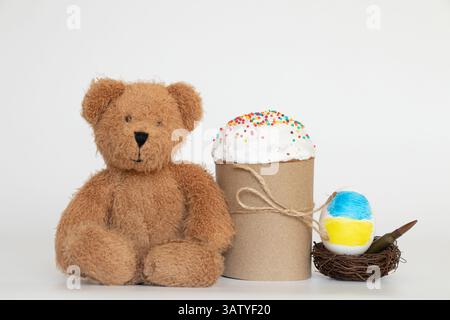 Die Flagge der Ukraine ist auf ein Ei gezeichnet, das in einem Nest mit einer Kugel liegt, und daneben gibt es einen Osterkuchen und einen Kinderteddybär, Ostern i Stockfoto