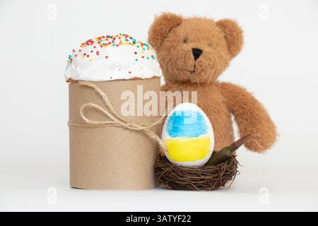 Die Flagge der Ukraine ist auf ein Ei gezeichnet, das in einem Nest mit einer Kugel liegt, und daneben gibt es einen Osterkuchen und einen Kinderteddybär, Ostern i Stockfoto
