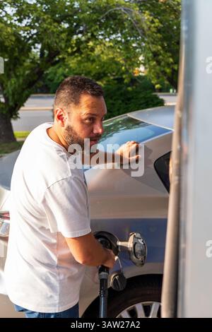 Ein Mann betankt sein Auto an einer Tankstelle. Er trägt ein weißes Hemd und blaue Jeans Stockfoto