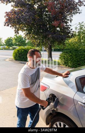 Ein Mann betankt sein Auto mit Benzin. Er trägt ein weißes Hemd und blaue Jeans Stockfoto
