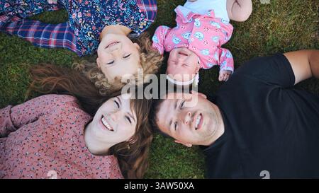 Glückliche vierköpfige Familie, die auf dem Gras liegt und an einem sonnigen Tag die gemeinsame Familienzeit genießt Stockfoto