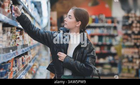 Eine junge Frau, die Lebensmittel auswählt, Regale durchsucht, frische Produkte kauft Stockfoto