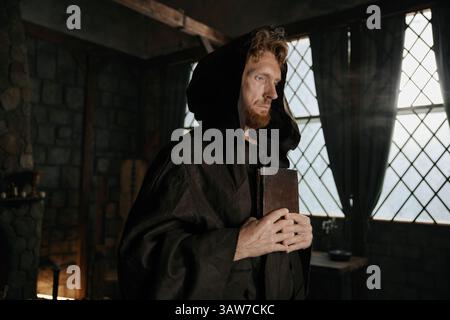 Mittelalterlicher Priester mit geschlossenem Bibelbuch und Rosenkranzperlen in der Hand Nahaufnahme Stockfoto