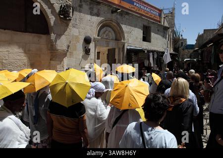 Rückansicht der äthiopisch-orthodoxen Pilger, die in einer Karfreitagsprozession auf der Via Dolorosa auf dem Weg nach Golgotha spazieren, einige benutzen gelbe Regenschirme. Stockfoto