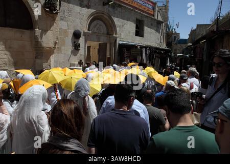 Rückansicht der äthiopisch-orthodoxen Pilger, die in einer Karfreitagsprozession auf der Via Dolorosa auf dem Weg nach Golgotha spazieren, einige benutzen gelbe Regenschirme. Stockfoto