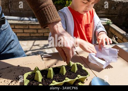 Erwachsene Pflanzen Samen, während das Kind sie im Hintergrund untersucht, ökologischer Gartenbau Stockfoto