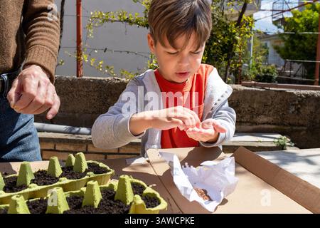 Kinder, die Samen pflanzenfertig halten, unter Anleitung von Erwachsenen in der Öko-Gartenarbeit Stockfoto