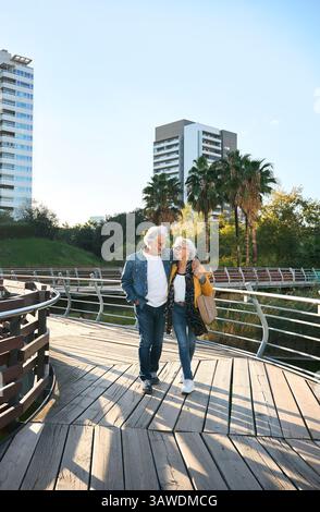 Glückliches Seniorenpaar, das auf einer Brücke in einem modernen Stadtpark spaziert Stockfoto