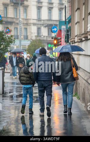 Eltern und Kind laufen im Regen auf der Straße, im Zentrum von Mailand. Stockfoto