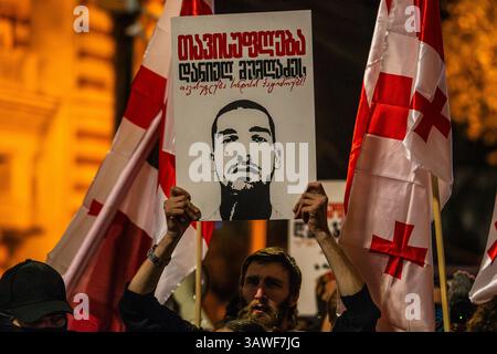 Tiflis, Georgien, 19. April 2025. Ein Demonstrant wirft ein Poster mit dem Porträt eines verhafteten Aktivisten auf. Georgische Fahnen winken um die Menge. Das Mem Stockfoto