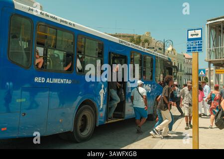 Havanna, Kuba 2024. April 17 - Passagiere steigen in einen blauen Alimentadora-Bus ein und verlassen ihn in der Mittagssonne am Terminal de Ferris. Dieser gemeinsame und erschwingliche öffentliche Bus Stockfoto
