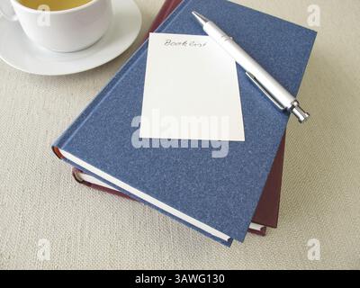 Ein Stapel Bücher, eine Liste mit Büchern und eine Tasse Tee Stockfoto