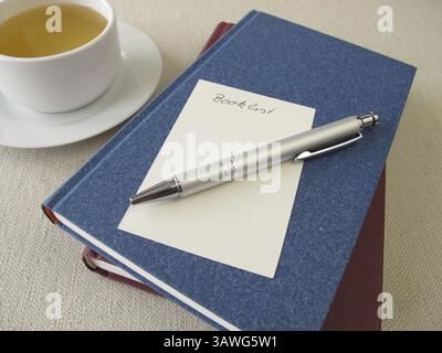 Ein Stapel Bücher, eine Liste mit Büchern und eine Tasse Tee Stockfoto
