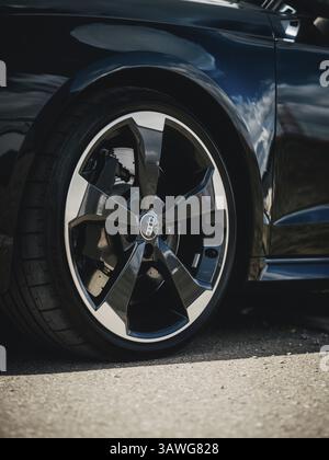 Nahaufnahme eines schwarzen Audi-Rads auf Asphaltboden bei Sonnenlicht Stockfoto