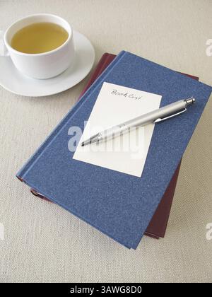 Ein Stapel Bücher, eine Liste mit Büchern und eine Tasse Tee Stockfoto